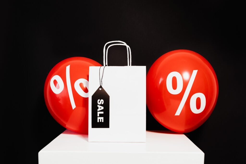Shopping bag with sale tag and percentage balloons on black background.